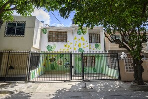 Un conjunto residencial amurallado con un edificio blanco que presenta diseños de hojas verdes y un portón de metal negro.