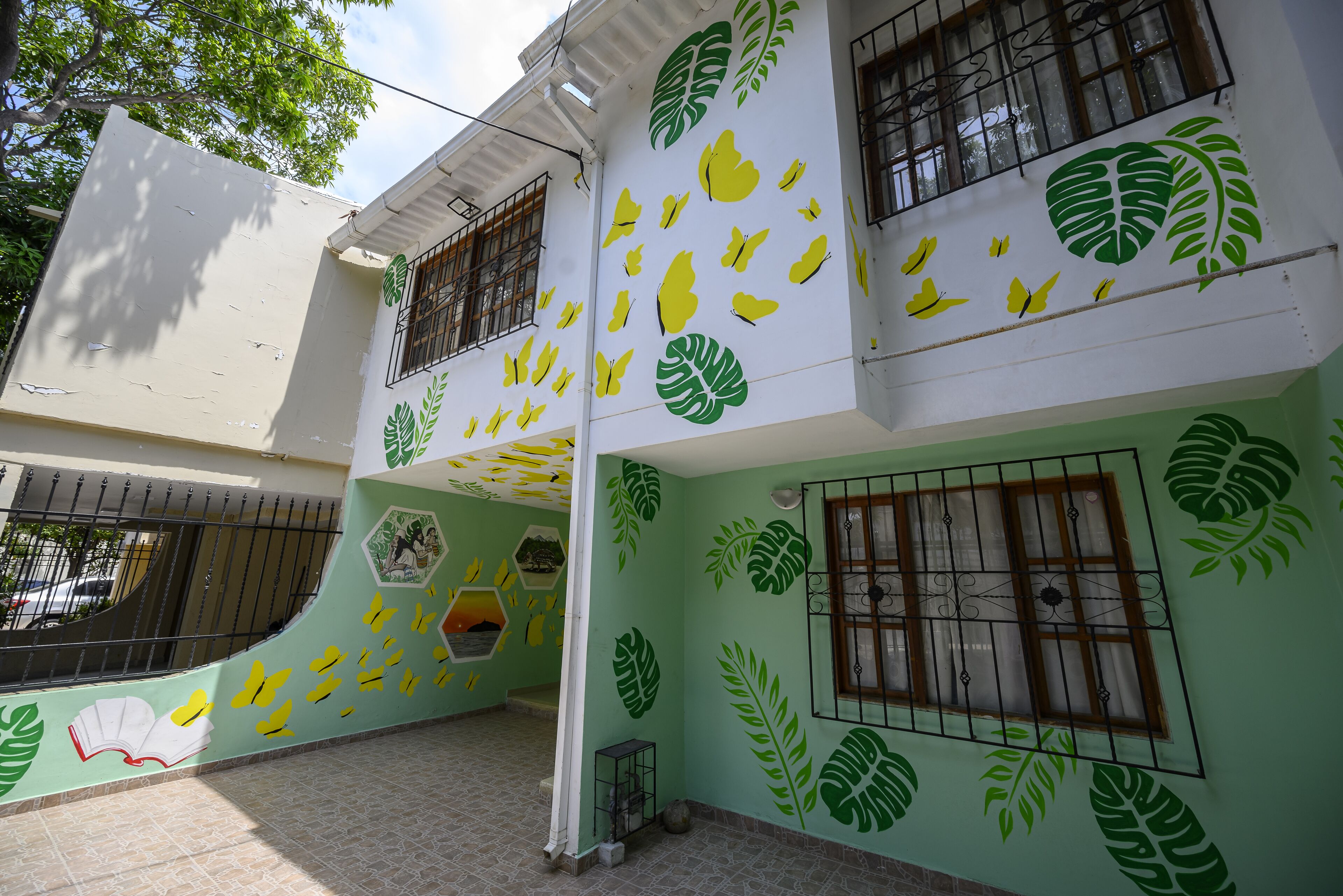 A building with green and yellow leaf patterns on the walls and a window with a metal grill.