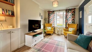 A living room with a television, two yellow armchairs, a sofa, a plaid rug, and a bookshelf. - 3 bedroom accommodation in Ceres, near Cupar (Ceres, near Cupar)