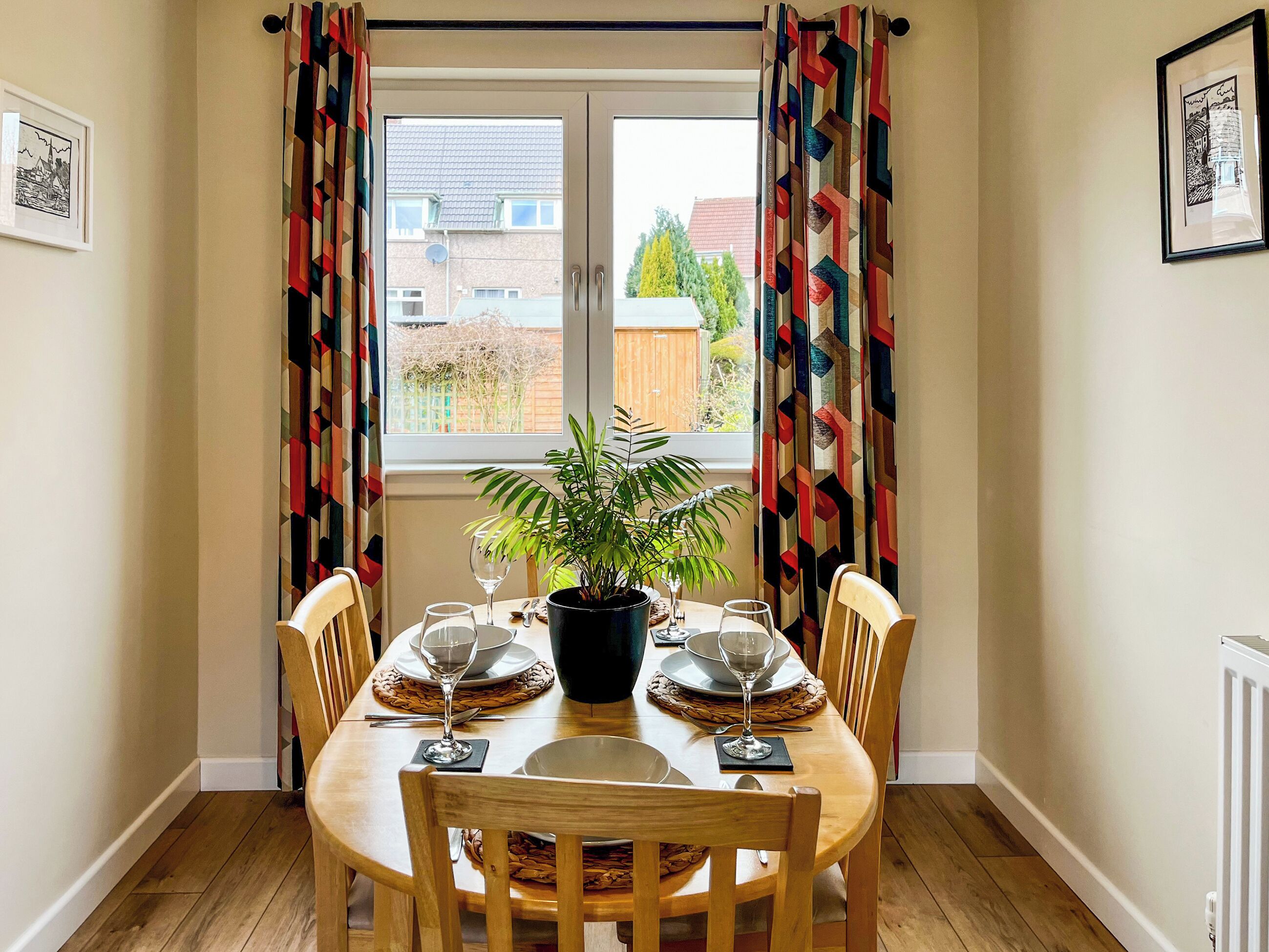 Un comedor con una mesa dispuesta para dos personas, una planta en maceta y vistas al exterior.