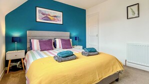 A bedroom with a bed, two bedside tables, a nightstand, a wall-mounted lamp, and a door. - 3 bedroom accommodation in Ceres, near Cupar (Ceres, near Cupar)