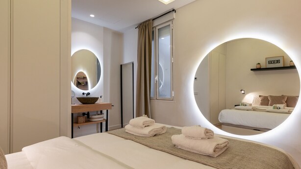 A modern hotel room with a large bed, a round mirror, a vanity with a bowl, and a shelf with a picture frame. - Nice studio 100 meters from Plaza de Callao (Madrid)