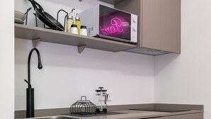 A modern kitchen with grey cabinets, a stainless steel sink, and a microwave on a shelf. - Nice studio 100 meters from Plaza de Callao (Madrid)