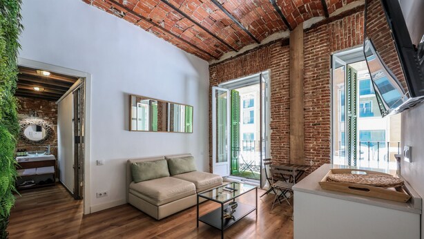 A modern living room with a wooden floor, a beige sofa, a glass coffee table, and a brick wall. - Cozy apartment in the Plaza de Callao (Madrid)