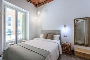 Un dormitorio con una cama, un banco, un espejo y una ventana con vistas a edificios.