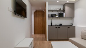 Een moderne keuken met grijze kastjes, een magnetron en een koffieapparaat. Er is een houten deur die naar een andere kamer leidt.