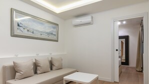 Een minimalistische woonkamer met een bank, een kleine tafel, een ingelijste schilderij en een airconditioning.