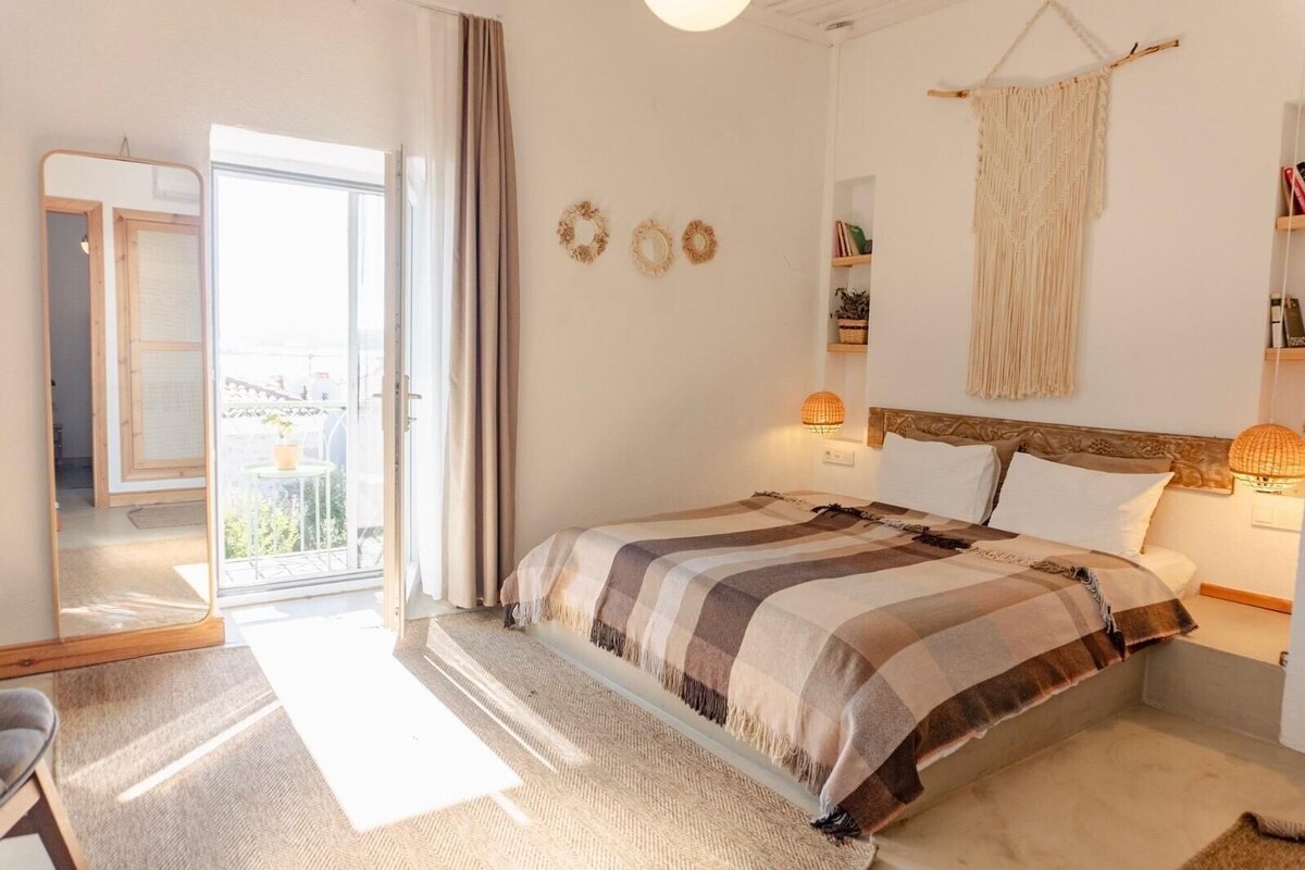 A bedroom with a bed, bedside lamps, a mirror, and a view of the outdoors.