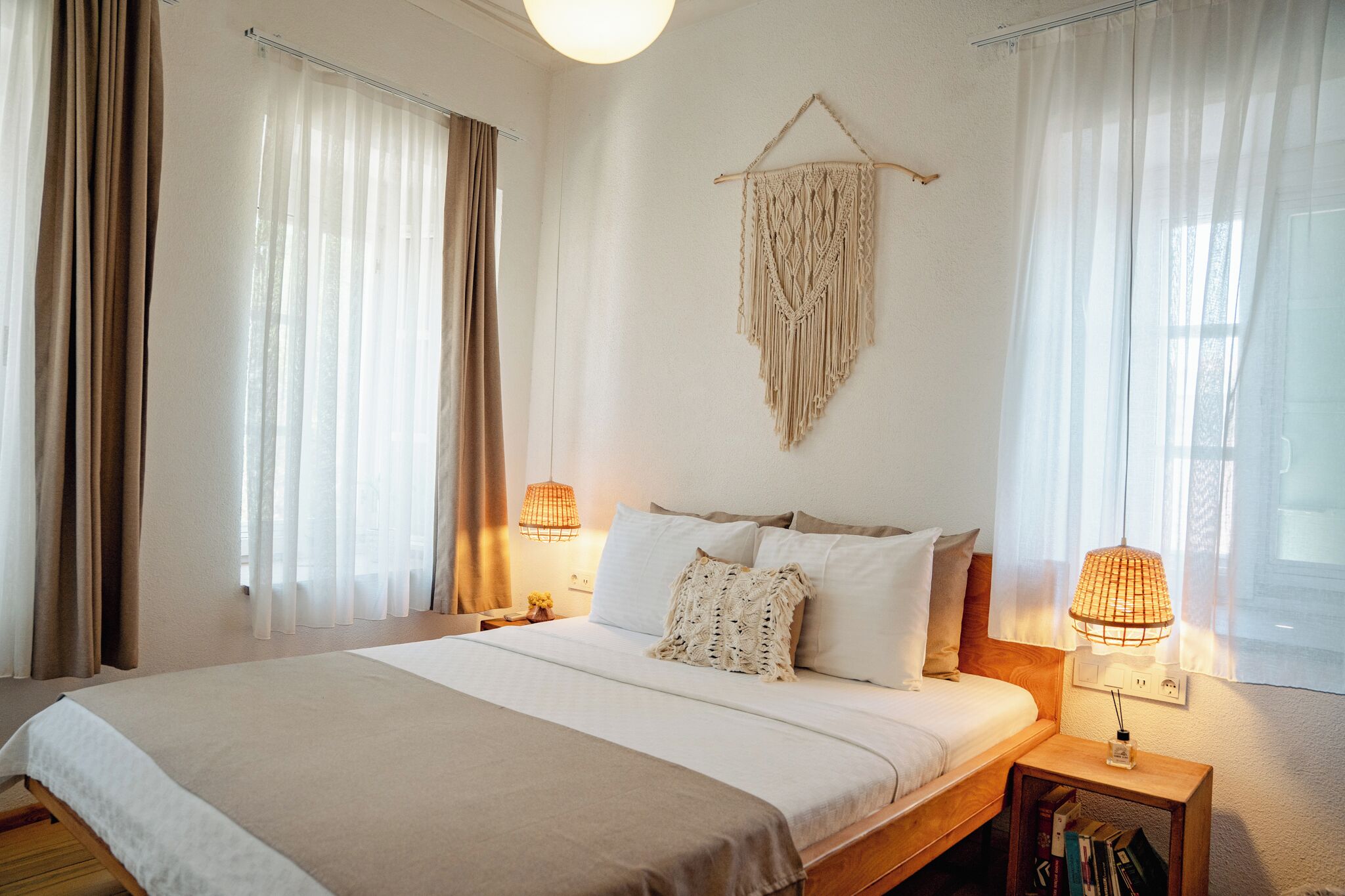 Una cama bien hecha con cabecera, dos lámparas de noche y un tapiz de macramé en la pared.