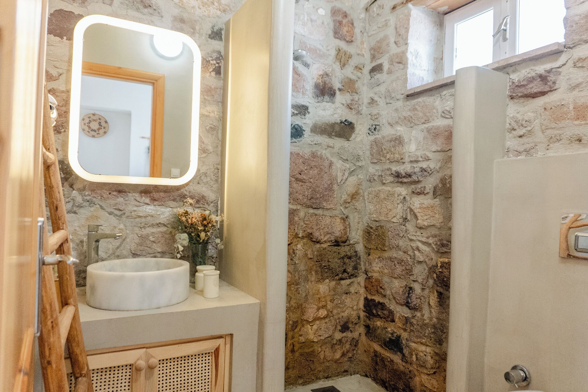 A bathroom with a stone wall, a round sink, a mirror, and a wooden ladder.