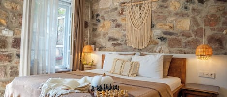 A bedroom with a stone wall, a bed with a wooden headboard, a chessboard, and a macrame wall hanging.