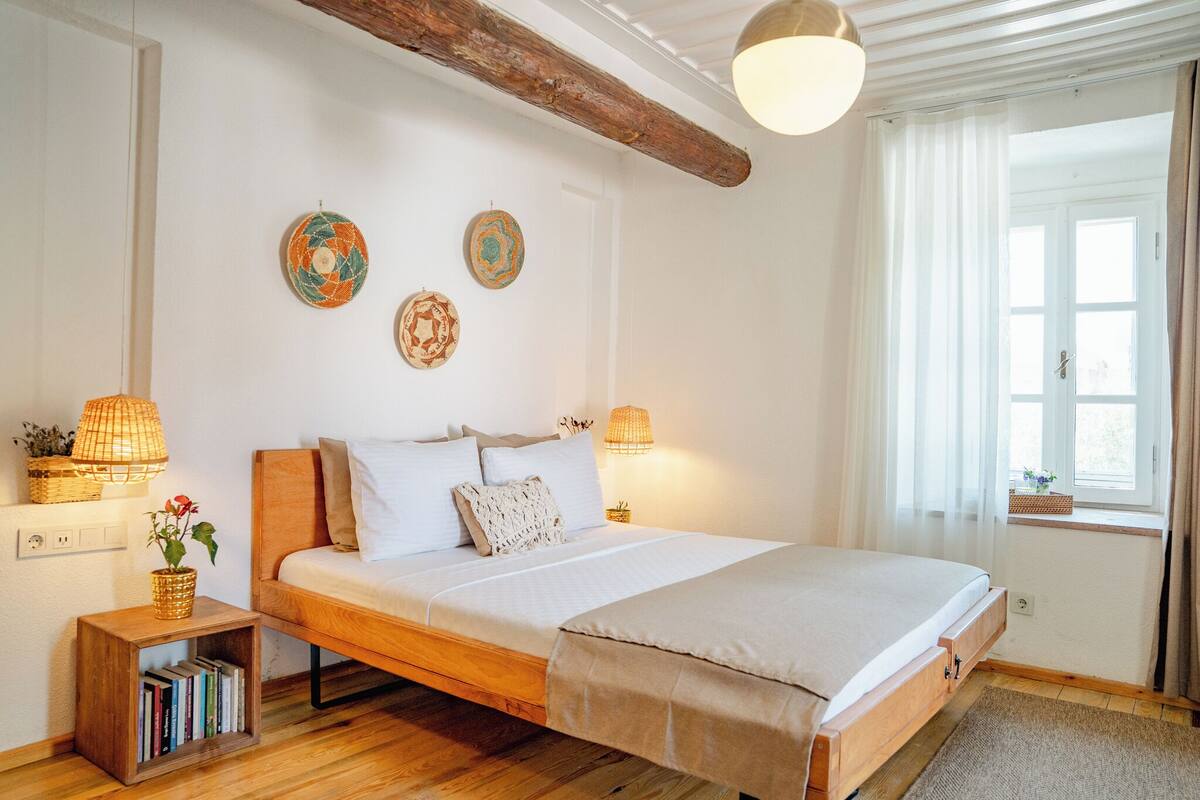 Une chambre à coucher avec un lit en bois, des lampes de chevet, une petite bibliothèque et des assiettes décoratives accrochées au mur.