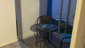 Een klein balkon met een glazen deur, een ronde tafel en twee stoelen.