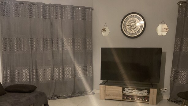Een woonkamer met een grote flatscreen televisie, een bank en een kamerkleurig gordijn.