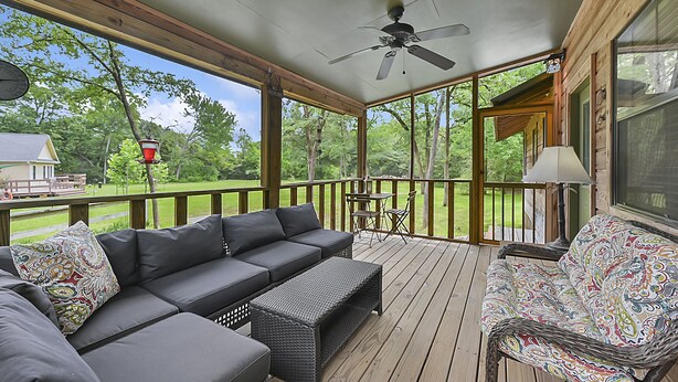 A covered outdoor deck with a sofa, a chair, and a table. - Retreat To Cardinals Cabin (Bryan)
