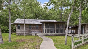 A rustic cabin with a porch, large windows, and a covered outdoor seating area. - Retreat To Cardinals Cabin (Bryan)