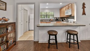 A modern kitchen with a central island, wooden cabinets, and a microwave. There are two stools at the island. - Retreat To Cardinals Cabin (Bryan)