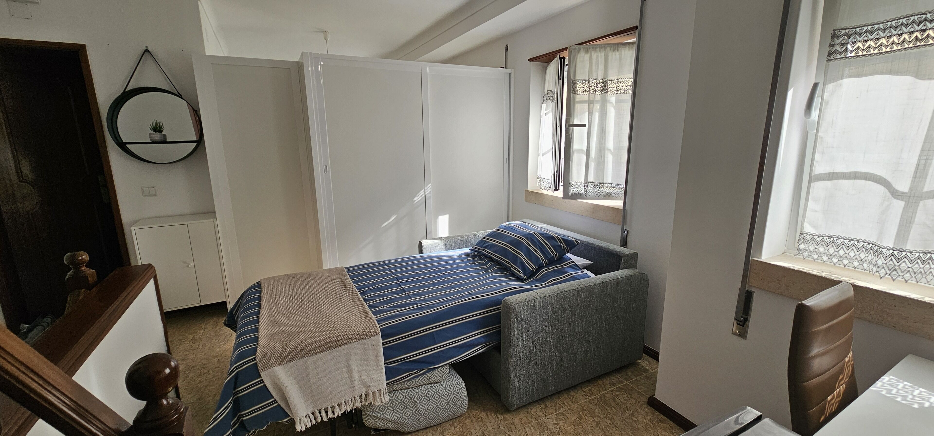 A bedroom with a bed, a window with curtains, a wardrobe, and a small plant on the wall.