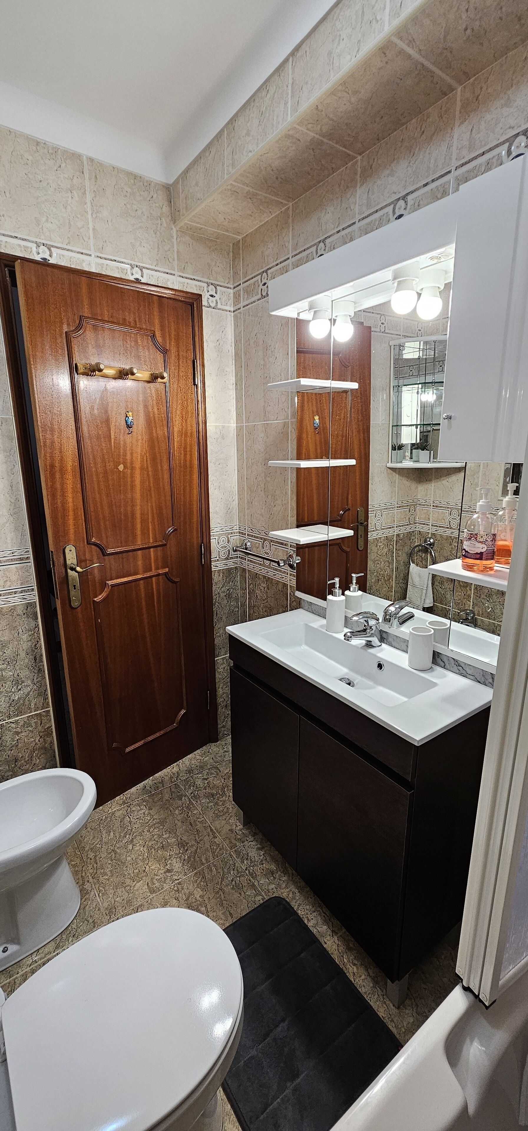 A bathroom with a wooden door, a white toilet, a large sink with a mirror, and a bathtub.