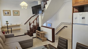 A living room with a sofa, a TV, a staircase, and a refrigerator. -  Sunao (Nazaré)
