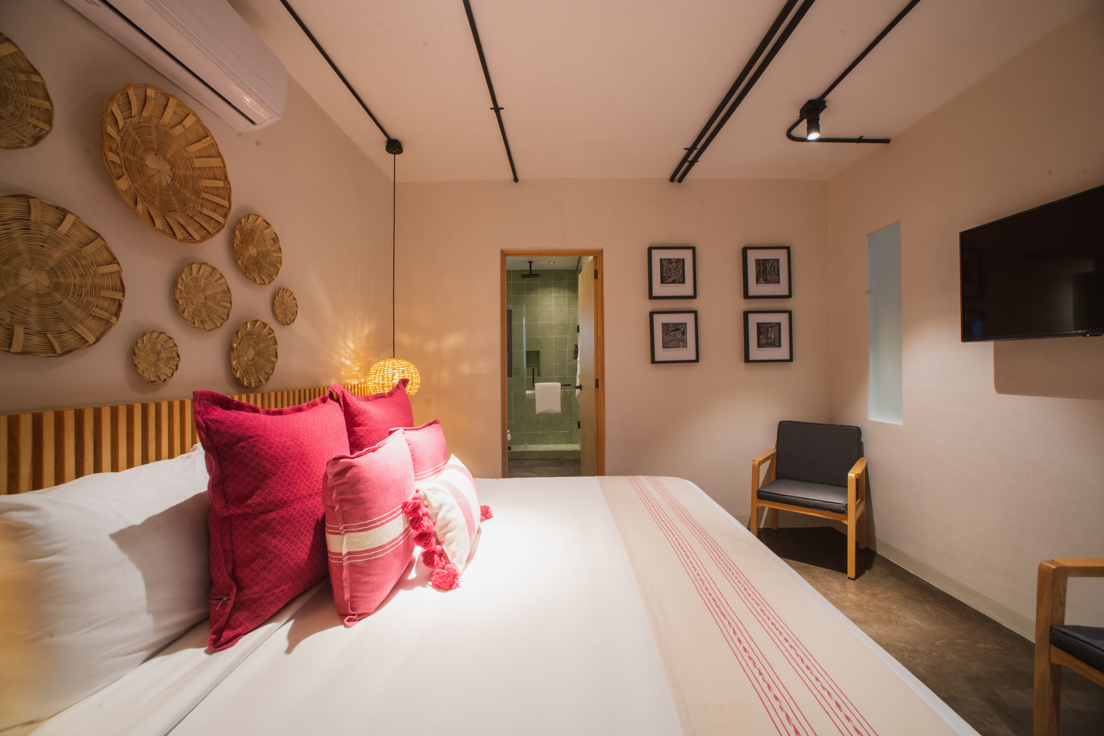 Een slaapkamer met een bed, kussens, een stoel, een televisie en decoratie aan de muur.