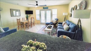 A living room with a dining area, a sofa, a TV, and a ceiling fan. - Gorgeous views, sleeps 6, clean, less than 100 steps to beach access.  (Destin)