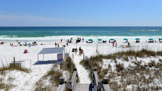 A beach with a wooden boardwalk leading to a lifeguard station, beach umbrellas, and people relaxing on the sand. - Gorgeous views, sleeps 6, clean, less than 100 steps to beach access.  (Destin)