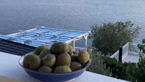 Uma tigela de fruta numa varanda com vista para um corpo de água e colinas ao longe.