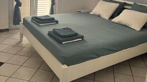 Uma cama bem arrumada com colcha e travesseiros verdes, cabeceira branca e janela com cortinas azuis.