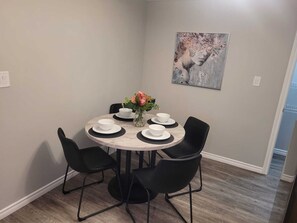 A dining area with a round table, six chairs, white plates, bowls, and a vase with flowers.