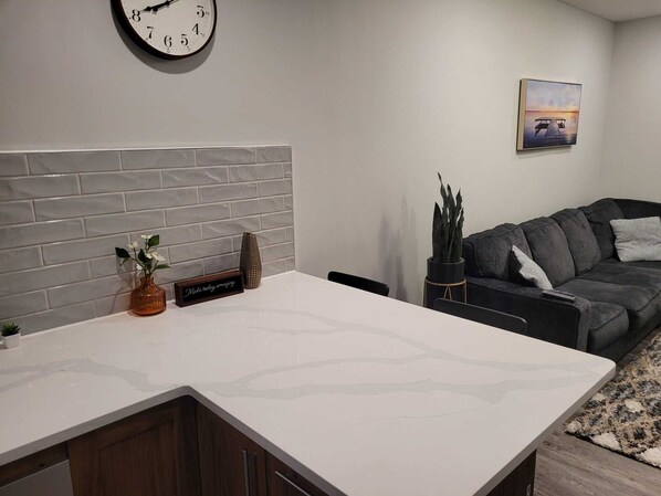 A modern kitchen with a white countertop, a clock on the wall, and a grey brick backsplash.
