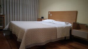 Ein ordentlich bezogenes Bett mit Steppdecke, einem Holzkopfschild und einem Nachttisch mit Lampe.