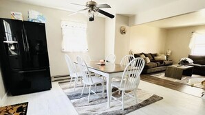 Una cocina moderna con un refrigerador negro, sillas blancas alrededor de una mesa de madera y un ventilador de techo.