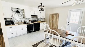 Una cocina moderna con armarios blancos, una mesa de comedor con sillas y una puerta de madera.