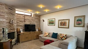 A living room with a stone wall, a flat-screen TV, a sofa, and a fireplace. - 1 Bedroom Villa in Noicattaro (Noicattaro)