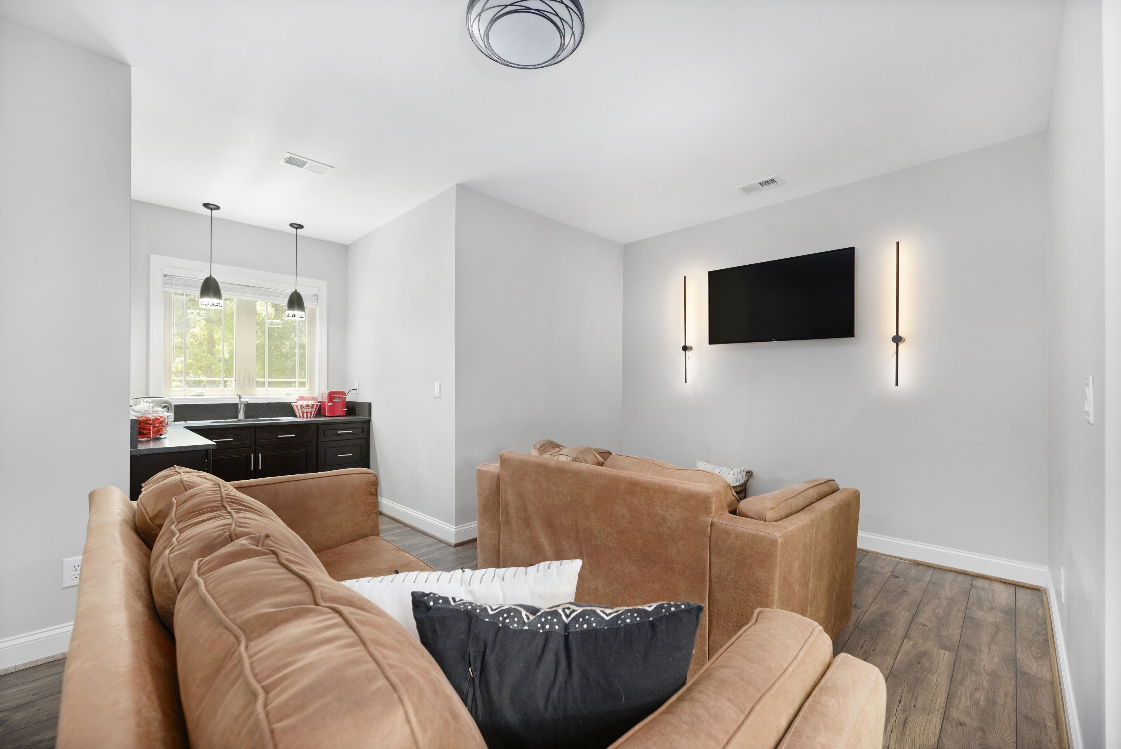 Una sala moderna con un juego de sofá, un televisor de pantalla plana montado en la pared y una cocina al fondo.