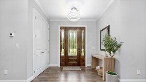 Un pasillo con puerta de madera, una lámpara, un banco y una planta en maceta.