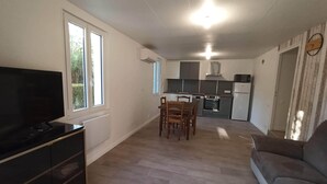 A modern kitchen with grey cabinets, a built-in oven, and a refrigerator. There is a dining area with a table and chairs, and a flat-screen TV on a stand. - Gîte au Calme en Quercy Entre Sarlat, Lascaux et Rocamadour (Souillac)
