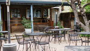 Ein Straßencafé mit Tischen, Stühlen und einer Speisekarte, im Hintergrund ein Holzzaun.