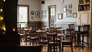 Ein Restaurantinneres mit Holztischen und -stühlen, gerahmten Bildern an den Wänden und einer weißen Tür.