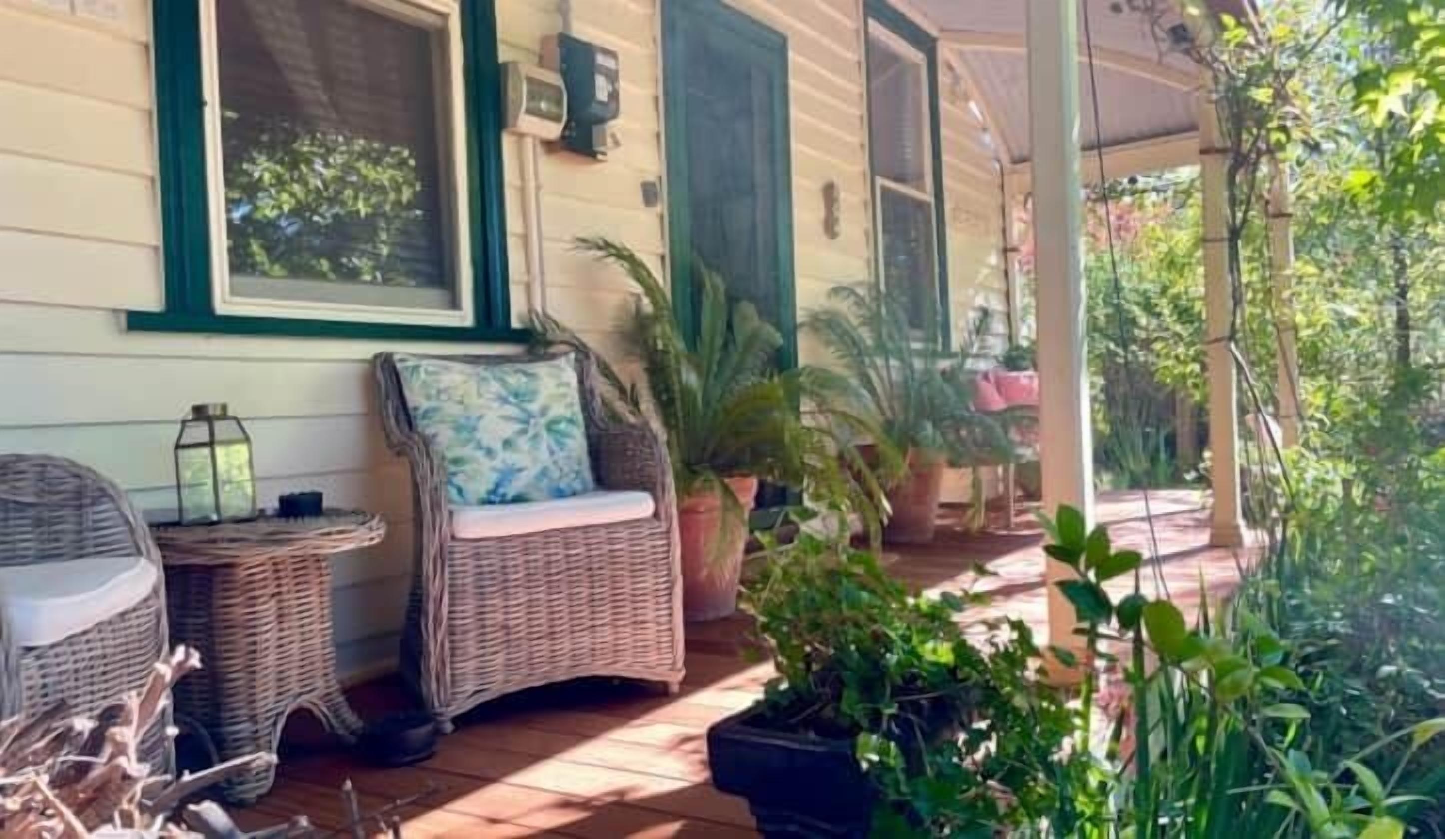 Une véranda aménagée avec des meubles en osier, des plantes en pot et une vue sur la verdure environnante.