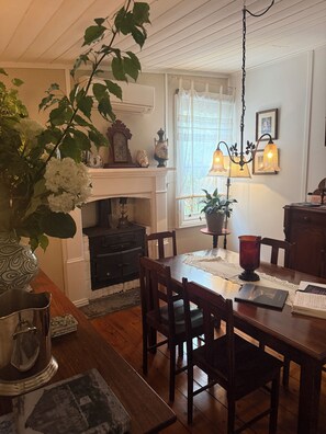A dining area with a wooden table, chairs, a vase with flowers, a fireplace, and a hanging light fixture.
