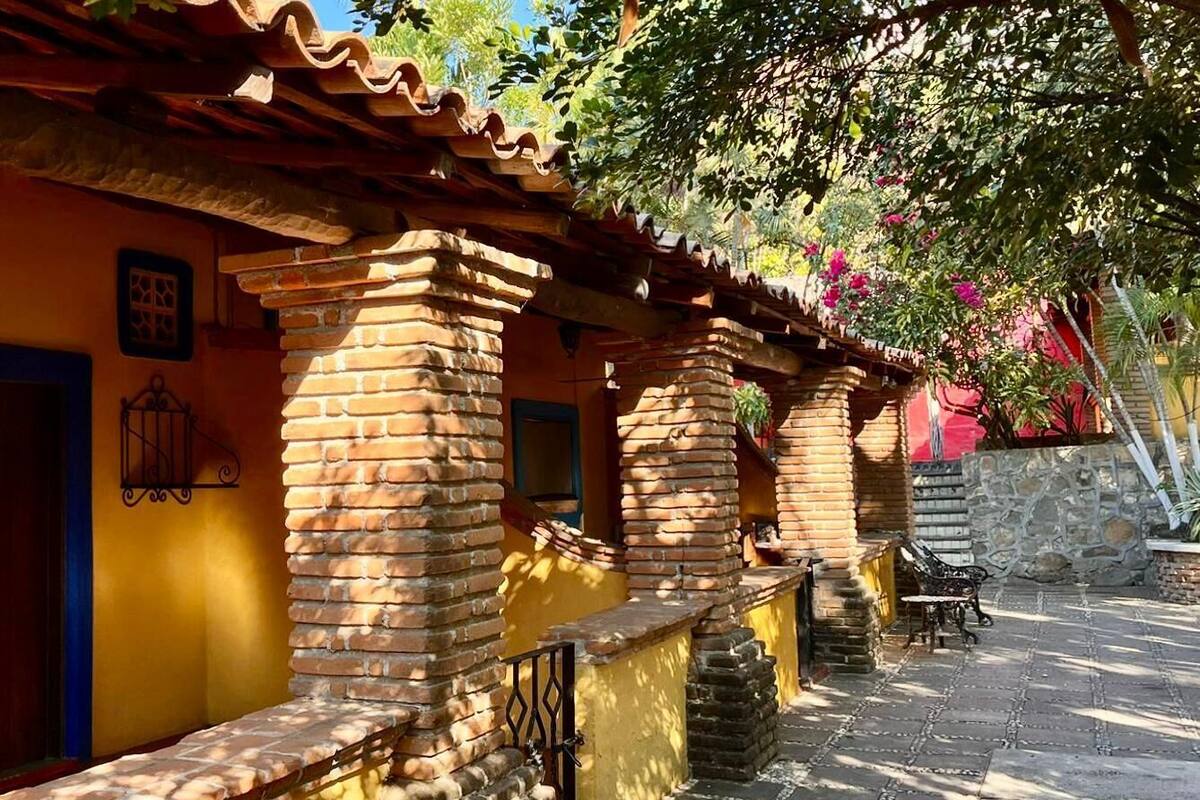 A courtyard with brick arches and a yellow wall, a stone bench, and a potted plant.