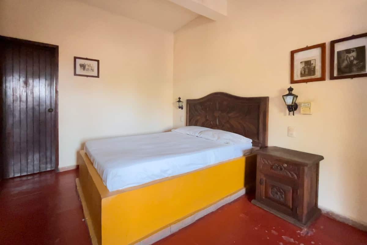 A room with a bed, a wooden nightstand, a door, and two wall-mounted light fixtures.