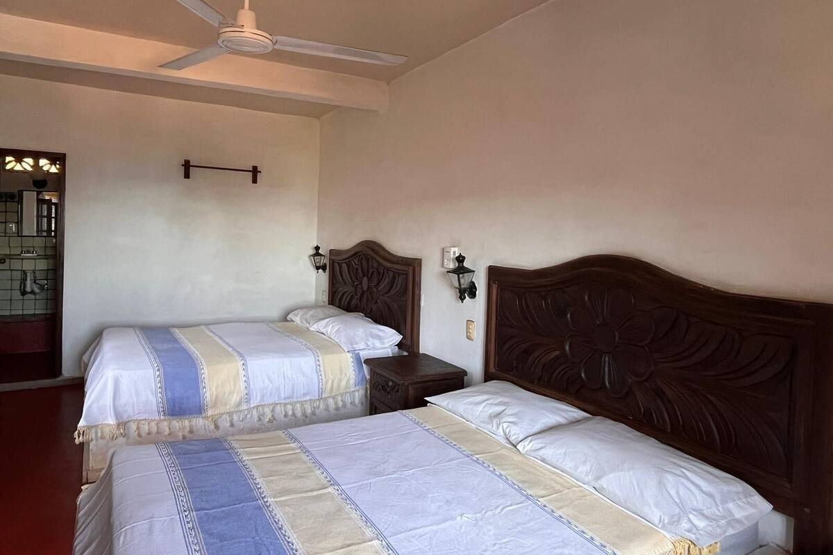 A hotel room with two beds, a ceiling fan, a nightstand, and a wall-mounted lamp.