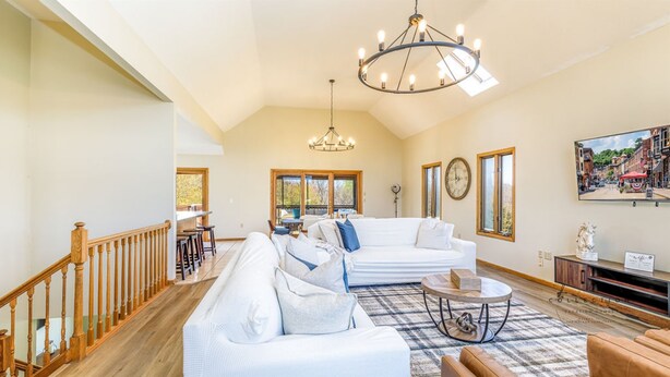 A spacious living room with a high ceiling, a large chandelier, a white sofa set, a coffee table, and a view of the outside through large windows. - Partridge Place | 4 Ensuite Bedrooms, Hot Tub, Fire Pit, Dog-Friendly (Galena)
