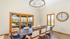 A dining area with a large table, chairs, and a chandelier. There are large windows and a view of the outdoors. - Partridge Place | 4 Ensuite Bedrooms, Hot Tub, Fire Pit, Dog-Friendly (Galena)