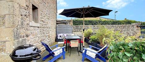 An outdoor patio with stone walls, a grill, blue chairs, and a table under a large umbrella.