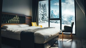 A bedroom with a bed, a chair, and a large window with a snowy mountain view. - Tuğra Butik Otel (Savsat)