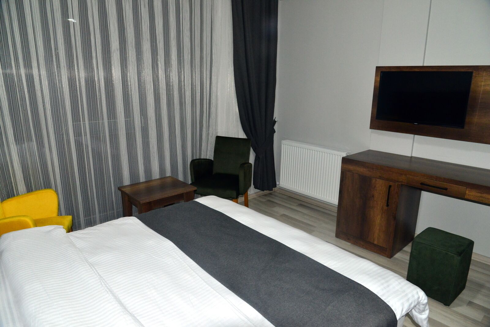 Una habitación de hotel con cama, escritorio, silla, televisor y radiador.